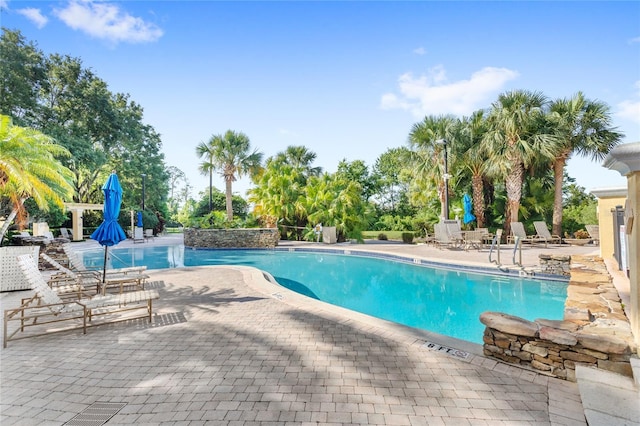 community pool with a patio area and view of wooded area