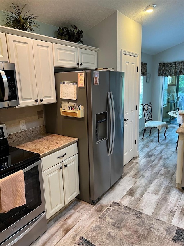 1121 Alcove Loop, The Villages, FL 32162 - kitchen featuring appliances with stainless steel finishes, light wood-style flooring, vaulted ceiling, white cabinets, and a textured ceiling