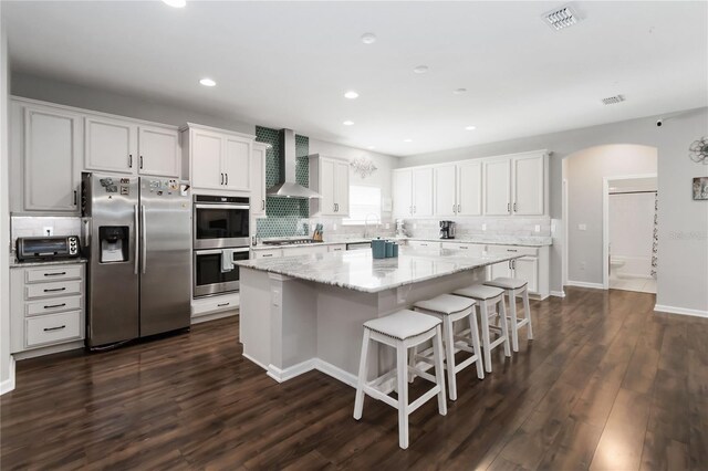1265 Blarney St, Minneola, FL 34715 - kitchen with stainless steel appliances, wall chimney exhaust hood, a kitchen island, backsplash, and arched walkways