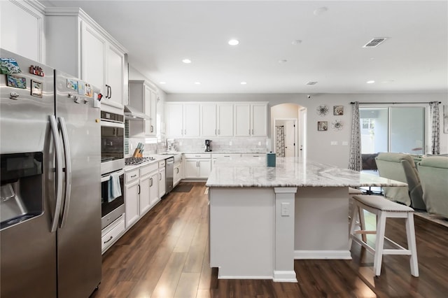 1265 Blarney St, Minneola, FL 34715 - kitchen featuring stainless steel appliances, open floor plan, dark wood-style flooring, arched walkways, and a center island