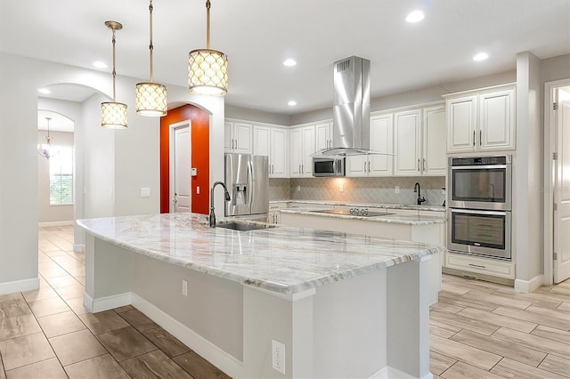 3844 Bowfin Trl, Kissimmee, FL 34746 - kitchen featuring stainless steel appliances, island exhaust hood, a large island with sink, arched walkways, and decorative backsplash