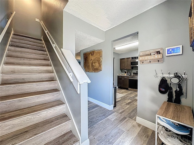 staircase with a textured ceiling, wood finished floors, and baseboards