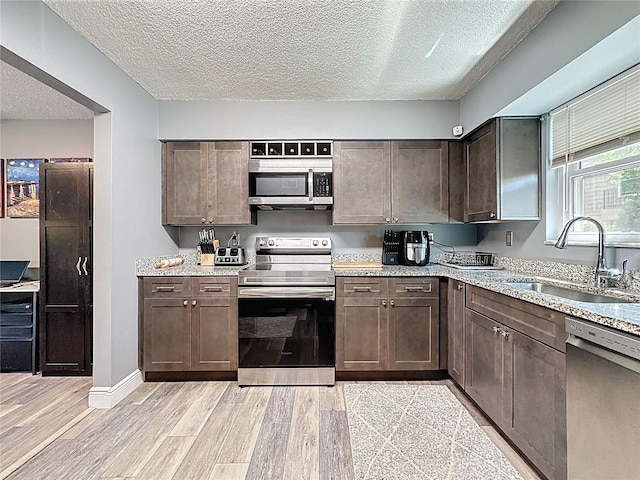 kitchen with stainless steel appliances, a sink, light wood finished floors, dark brown cabinets, and a textured ceiling
