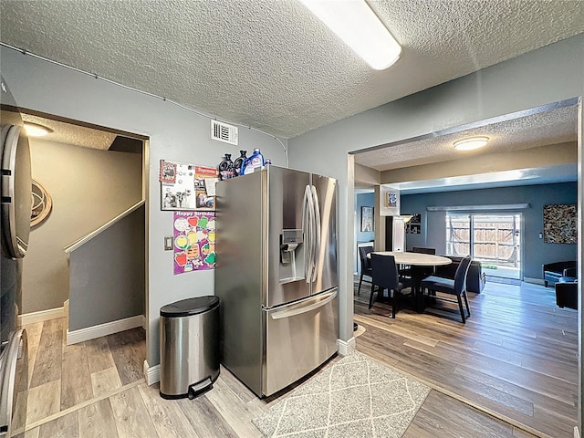 kitchen featuring stainless steel fridge, a textured ceiling, light wood-type flooring, and baseboards