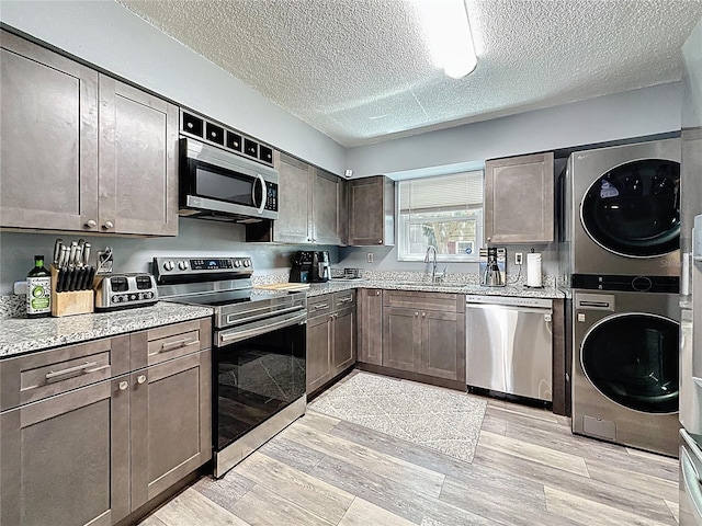 kitchen featuring stainless steel appliances, stacked washer and clothes dryer, a sink, a textured ceiling, and light wood-style floors