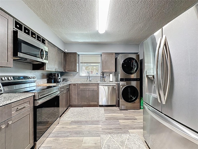 kitchen with appliances with stainless steel finishes, estacked washer and dryer, a textured ceiling, light wood finished floors, and dark brown cabinetry