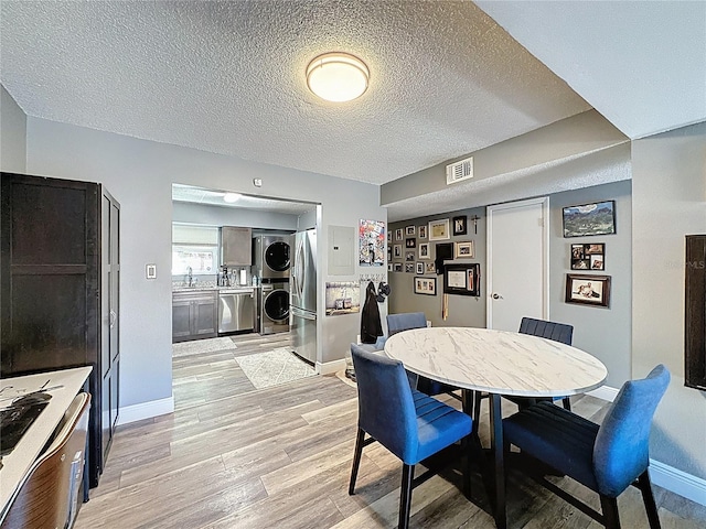 dining room with stacked washer and clothes dryer, light wood-style flooring, a textured ceiling, and baseboards