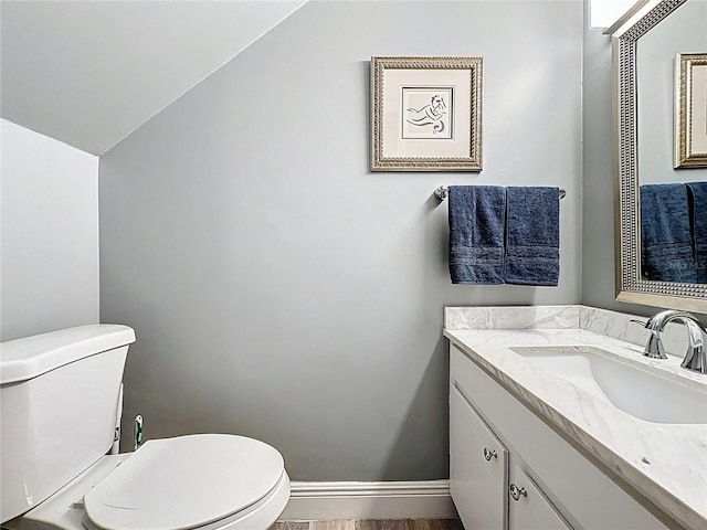 half bathroom featuring toilet, lofted ceiling, vanity, wood finished floors, and baseboards