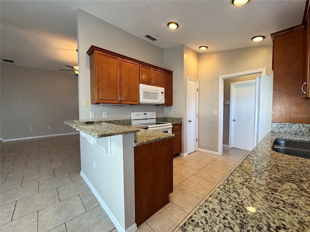703 Tartan Loop, Lake Wales, FL 33853 - kitchen with white appliances, stone countertops, light tile patterned flooring, brown cabinets, and a peninsula