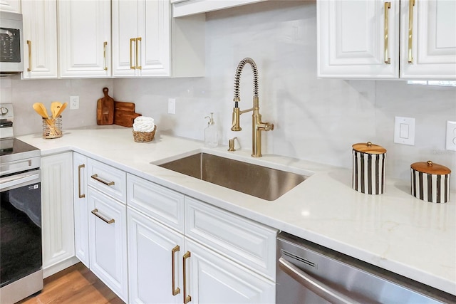 6700 Tamarind Cir, Orlando, FL 32819 - kitchen with appliances with stainless steel finishes, a sink, white cabinets, and wood finished floors