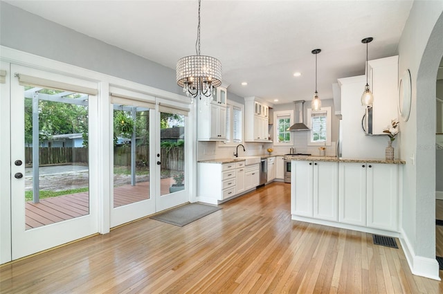 338 E Anderson St, Orlando, FL 32801 - kitchen featuring wall chimney range hood, appliances with stainless steel finishes, light wood-type flooring, white cabinetry, and recessed lighting
