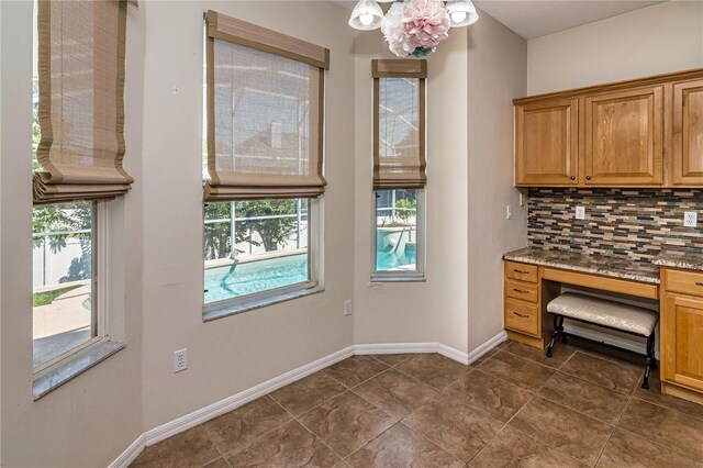 1201 Shelter Rock Rd, Orlando, FL 32835 - kitchen featuring backsplash, built in desk, stone countertops, dark tile patterned flooring, and a chandelier