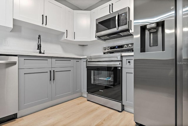 3926 Helena St NE, Saint Petersburg, FL 33703 - kitchen featuring appliances with stainless steel finishes, light wood-style floors, tasteful backsplash, gray cabinetry, and light stone counters