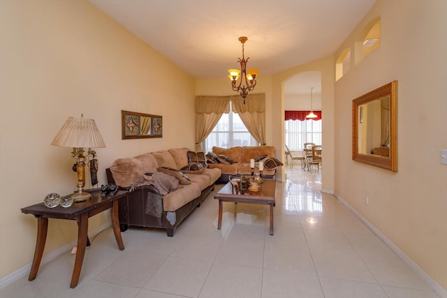 living room featuring a chandelier, light tile patterned floors, baseboards, and arched walkways