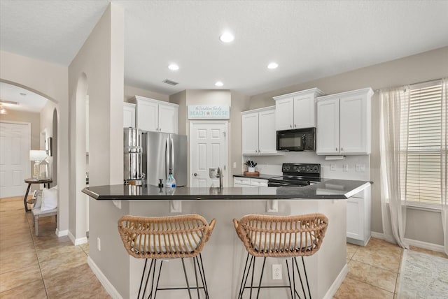 kitchen featuring black appliances, arched walkways, a breakfast bar, dark countertops, and recessed lighting