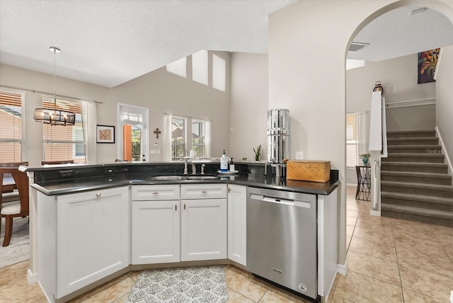 kitchen with stainless steel dishwasher, a sink, light tile patterned floors, dark countertops, and lofted ceiling