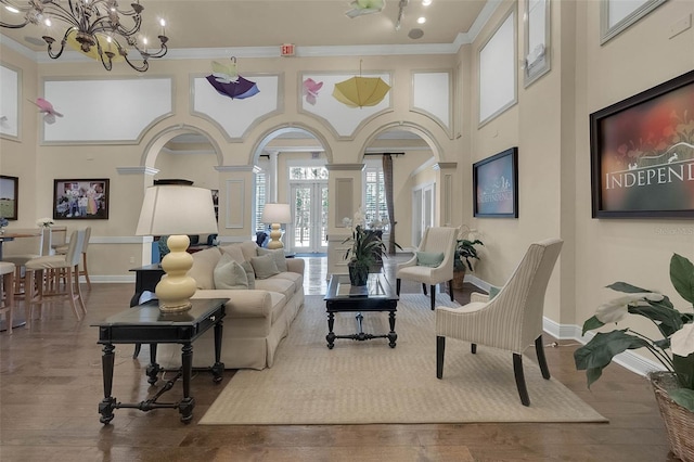 living area with a chandelier, a towering ceiling, wood finished floors, ornamental molding, and baseboards