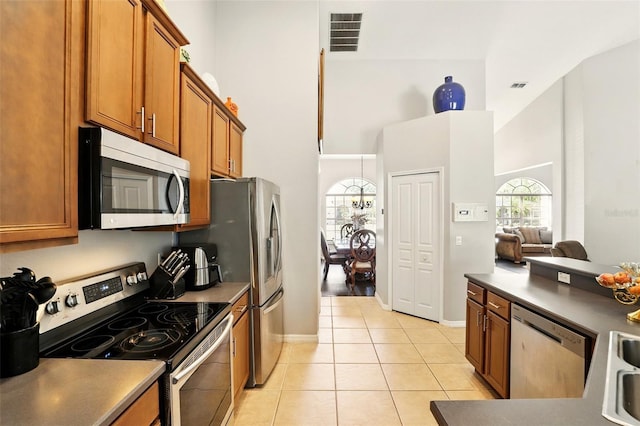 3451 Players Point Loop, Apopka, FL 32712 - kitchen featuring stainless steel appliances, a towering ceiling, brown cabinetry, light tile patterned floors, and dark countertops