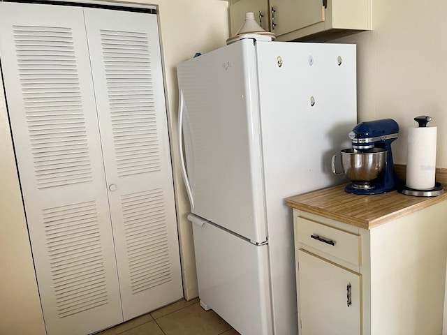kitchen featuring freestanding refrigerator, light tile patterned floors, light countertops, and white cabinets