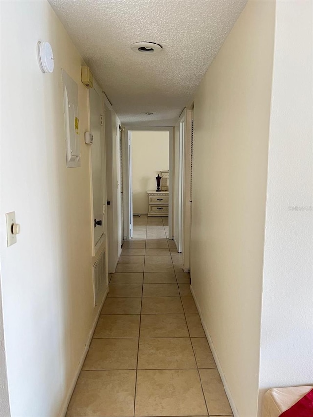 hallway with light tile patterned flooring, a textured ceiling, and baseboards
