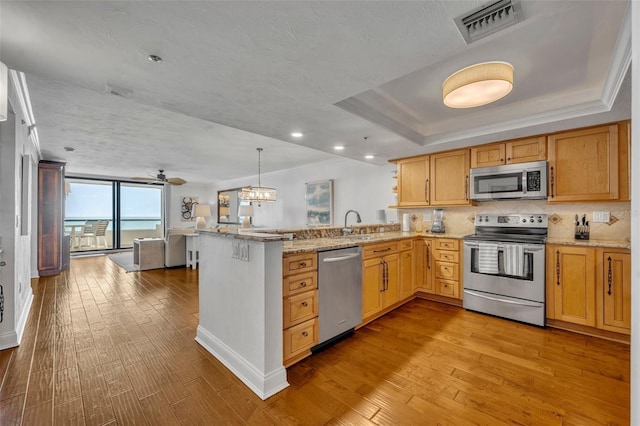 5275 S Atlantic Ave Unit 506, New Smyrna Beach, FL 32169 - kitchen featuring stainless steel appliances, a peninsula, a tray ceiling, hardwood / wood-style floors, and light stone countertops