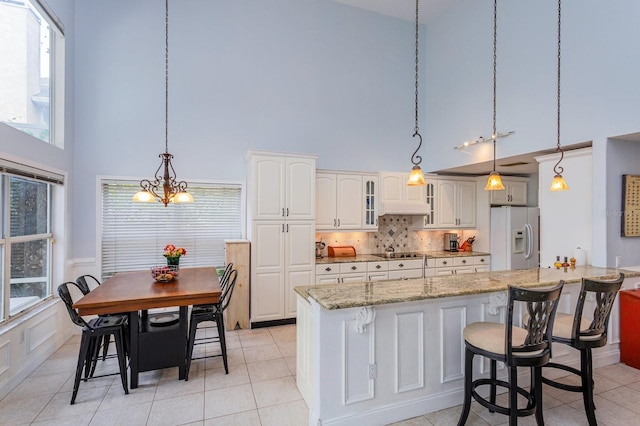 334 N Shadowbay Blvd, Longwood, FL 32779 - kitchen featuring white fridge with ice dispenser, a towering ceiling, black electric cooktop, light stone counters, and hanging light fixtures
