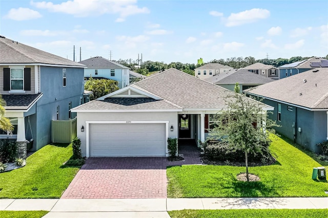 view of front of house with an attached garage, decorative driveway, a shingled roof, a residential view, and a front yard