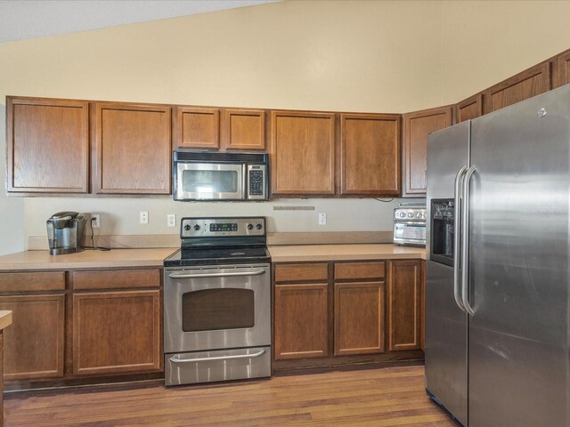 10247 Mason Loop, Clermont, FL 34711 - kitchen featuring appliances with stainless steel finishes, light countertops, vaulted ceiling, wood finished floors, and brown cabinetry