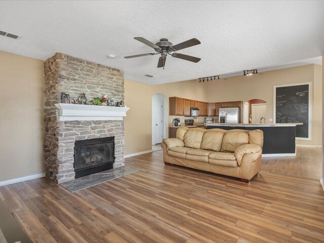 10247 Mason Loop, Clermont, FL 34711 - living area featuring arched walkways, a ceiling fan, a fireplace, light wood-type flooring, and a textured ceiling