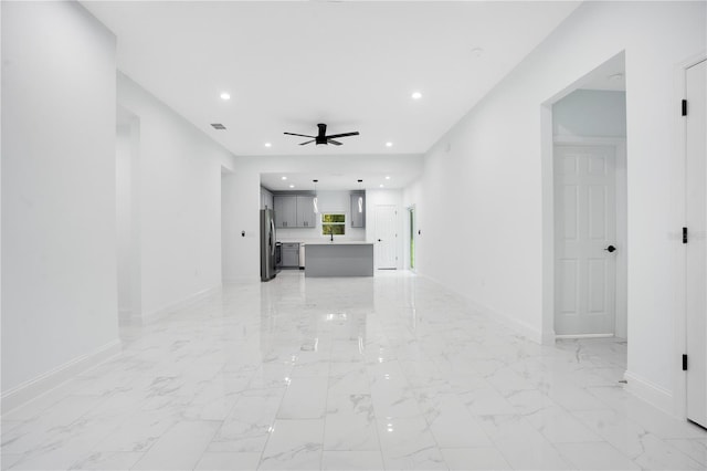 unfurnished living room with a ceiling fan, baseboards, recessed lighting, and light marble finish floors