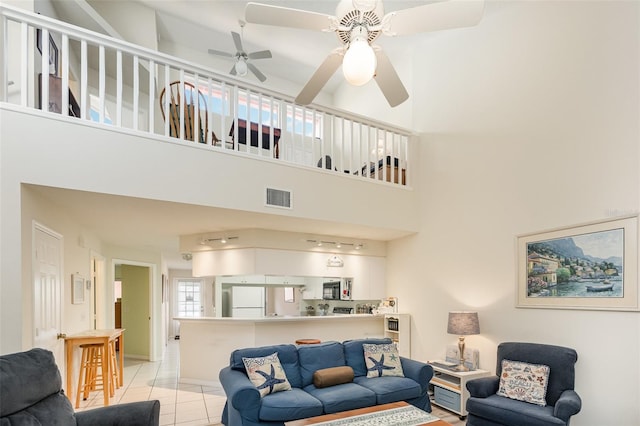 living area with ceiling fan, a towering ceiling, and light tile patterned floors