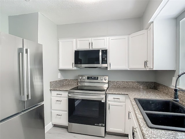 8228 Shriver Dr, Orlando, FL 32822 - kitchen with appliances with stainless steel finishes, a sink, white cabinetry, light wood finished floors, and a textured ceiling