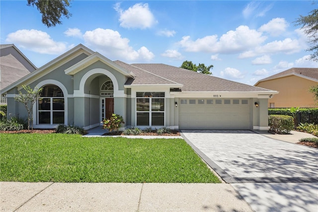 view of front of property with stucco siding, an attached garage, a front yard, decorative driveway, and a shingled roof