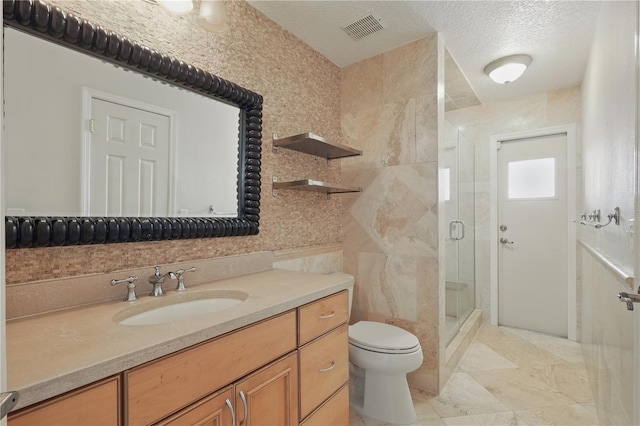 bathroom with toilet, a stall shower, vanity, a textured ceiling, and tile walls