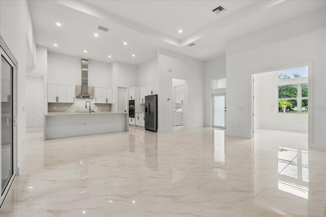 4528 Yorkshire Ln, Kissimmee, FL 34758 - kitchen featuring black fridge with ice dispenser, a high ceiling, wall chimney exhaust hood, open floor plan, and light marble finish floors