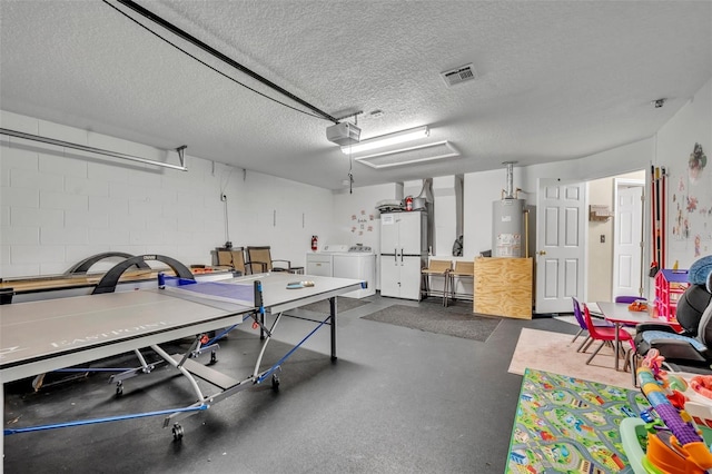 game room featuring washing machine and dryer, a garage, water heater, concrete block wall, and a textured ceiling
