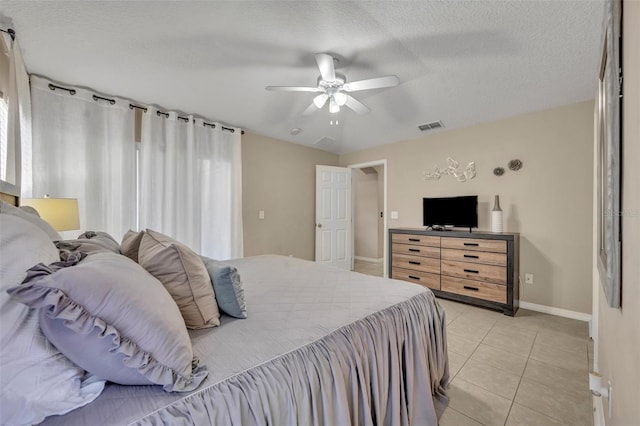 bedroom with baseboards, light tile patterned floors, a textured ceiling, and a ceiling fan