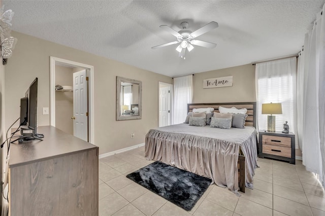 bedroom with light tile patterned floors, a textured ceiling, ceiling fan, baseboards, and a walk in closet