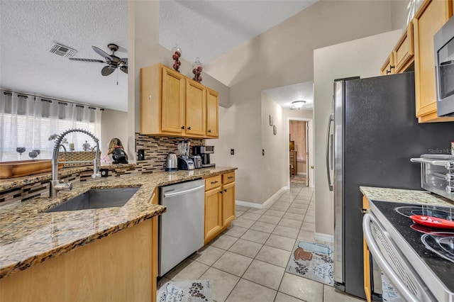 kitchen featuring appliances with stainless steel finishes, a sink, light brown cabinets, tasteful backsplash, and ceiling fan