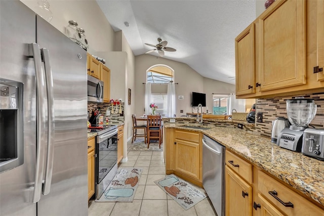 kitchen featuring appliances with stainless steel finishes, a sink, vaulted ceiling, tasteful backsplash, and a peninsula