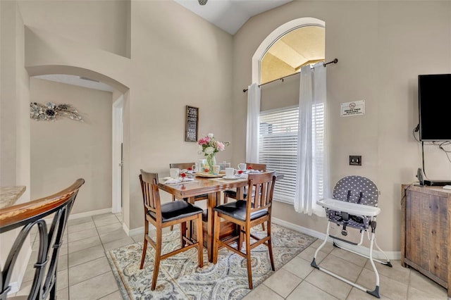 dining room with arched walkways, light tile patterned floors, baseboards, and high vaulted ceiling