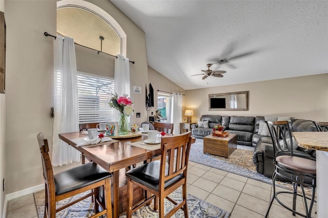 dining space with light tile patterned flooring, ceiling fan, vaulted ceiling, and a textured ceiling