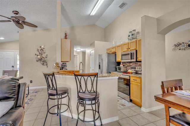 kitchen with appliances with stainless steel finishes, lofted ceiling, a kitchen bar, light tile patterned floors, and a ceiling fan