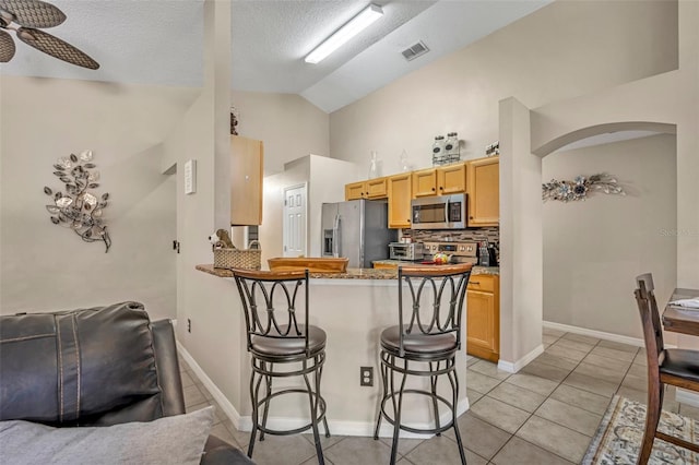 kitchen with stainless steel appliances, a kitchen breakfast bar, decorative backsplash, light tile patterned floors, and a peninsula