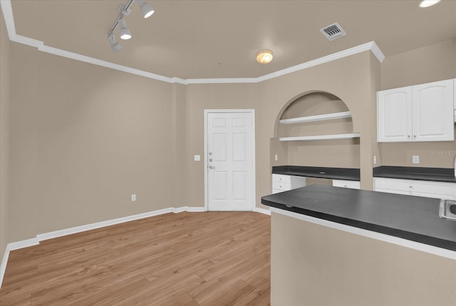 kitchen with dark countertops, white cabinets, crown molding, rail lighting, and light wood-type flooring