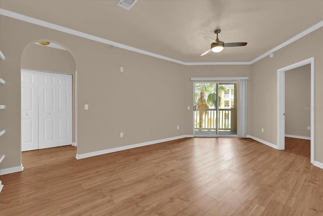 spare room featuring a ceiling fan, arched walkways, light wood finished floors, crown molding, and baseboards