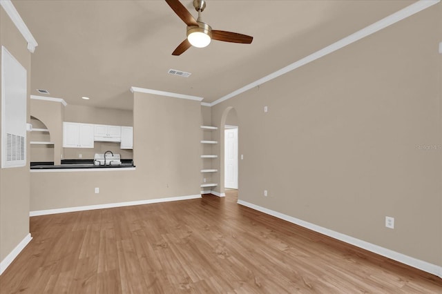 unfurnished living room with crown molding, arched walkways, a ceiling fan, a sink, and light wood-style flooring