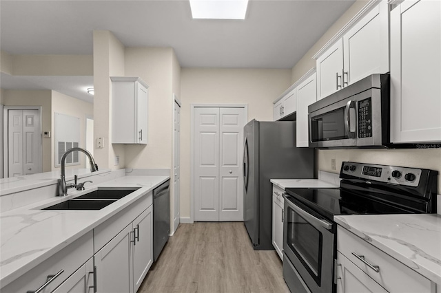 5447 Vineland Rd Unit 1308, Orlando, FL 32811 - kitchen with stainless steel appliances, a sink, light wood-style floors, white cabinetry, and light stone countertops