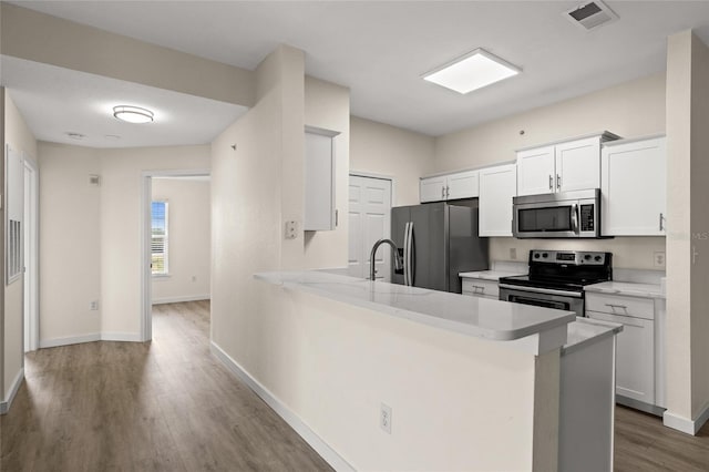 5447 Vineland Rd Unit 1308, Orlando, FL 32811 - kitchen featuring stainless steel appliances, wood finished floors, light countertops, white cabinetry, and a peninsula