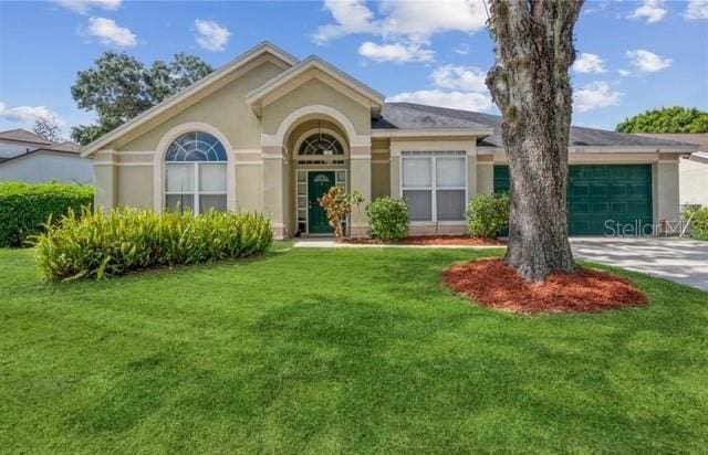 view of front of property featuring an attached garage, a front lawn, stucco siding, and driveway